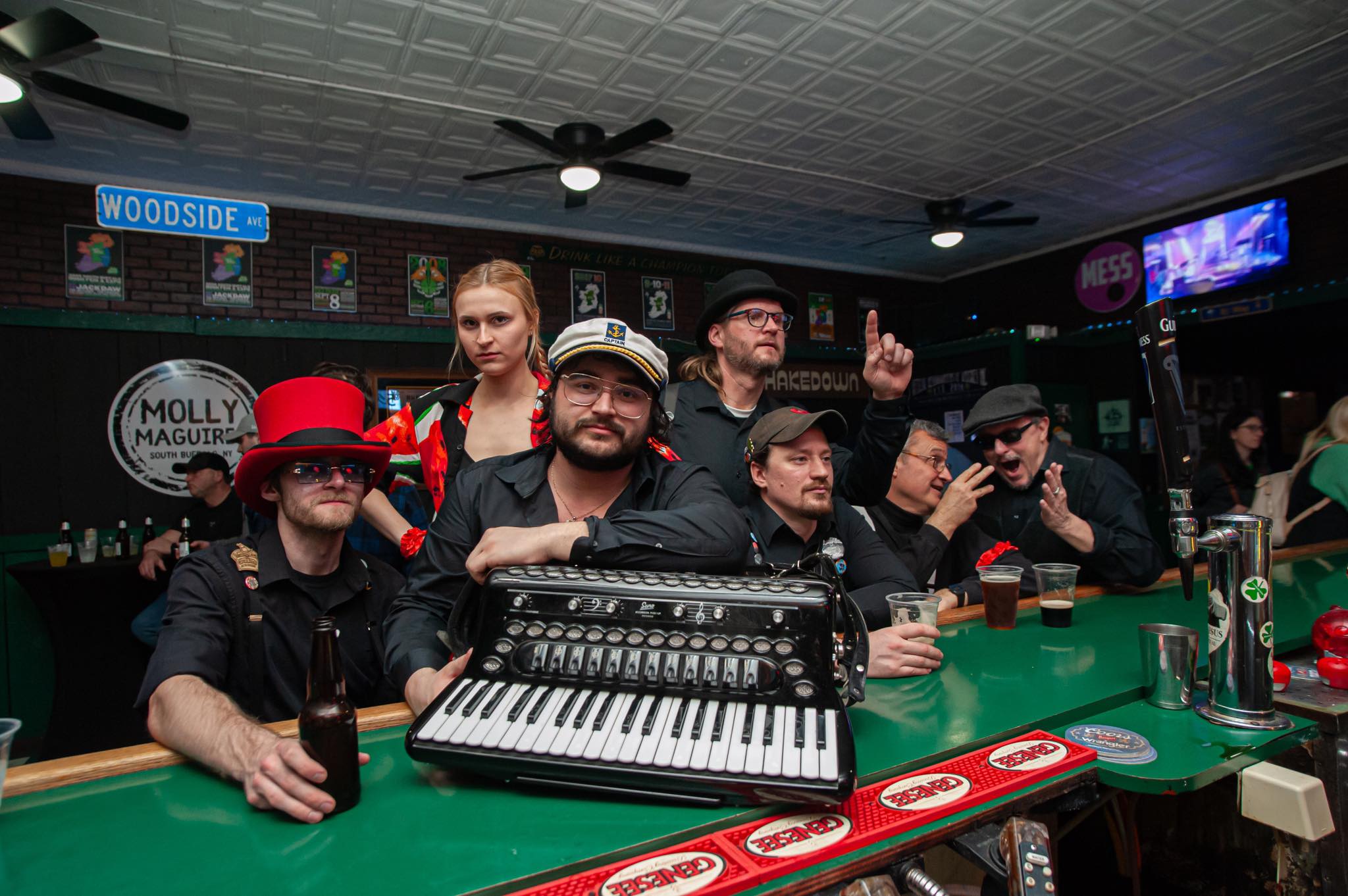Captain Tom, centered with an accordion, and the Hooligans gathered in a Buffalo tavern